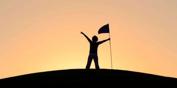 Shadow figure on orange background with hands in the air holding a flag