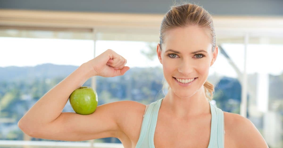 Healthy woman happy and smiling with an apple between her bicep and forearm
