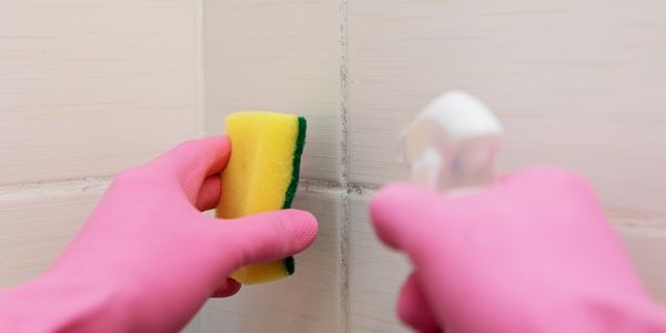Dirty tile cleaning and mould removal from grout while wearing rubber gloves for protection.