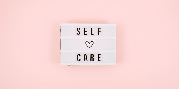 Self care with a heart in the middle on a pink background