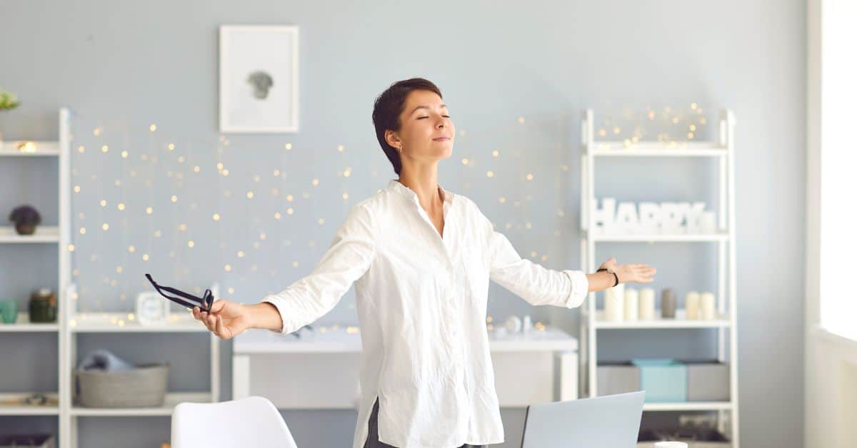 Woman standing in a room practicing mindfulness meditation with arms out and eyes closed